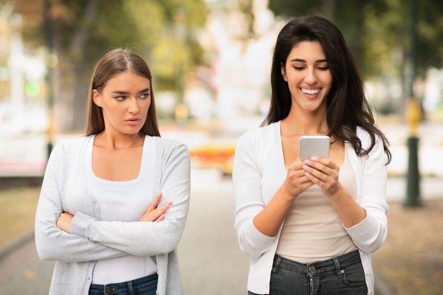 Two women walking down the street with one looking jealous and one looking very happy.