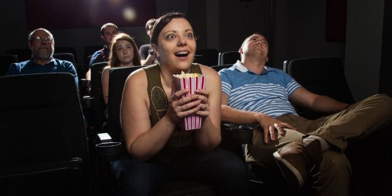 A woman sitting on the edge of her seat watching a movie and her face is filled with inspiration.